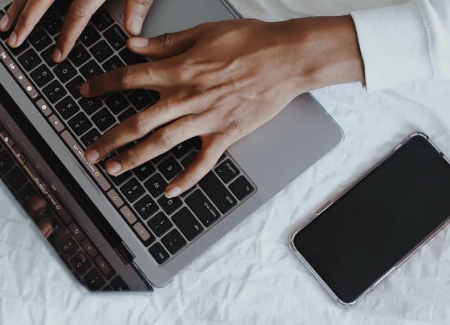 two hands on a laptop keyboard with a mobile phone next to it